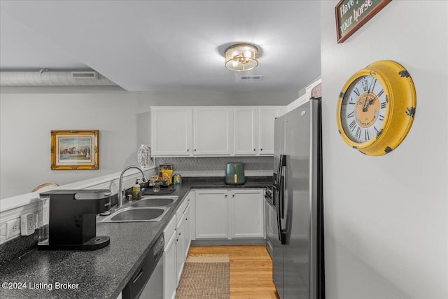 kitchen with stainless steel appliances, white cabinetry, backsplash, sink, and light hardwood / wood-style flooring