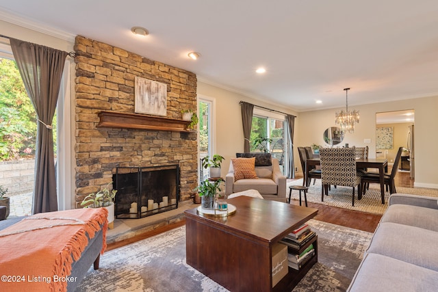 living room featuring a stone fireplace, an inviting chandelier, hardwood / wood-style floors, and crown molding