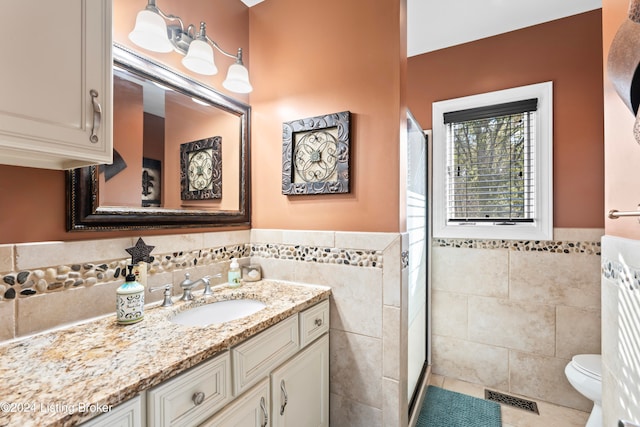 bathroom with tile walls, a shower with door, vanity, tile patterned flooring, and toilet