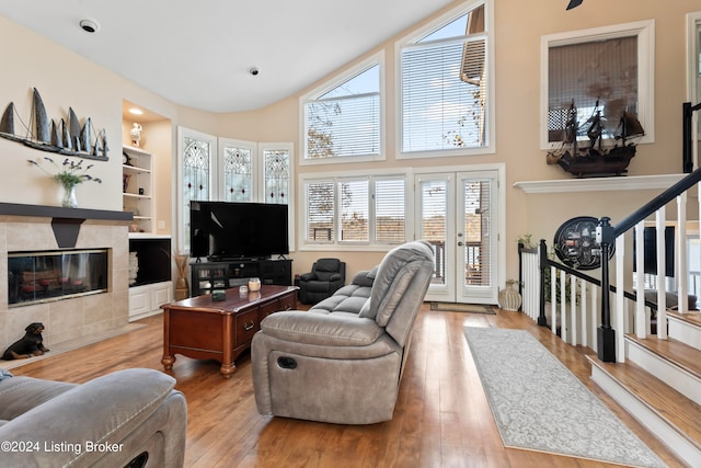 living room featuring built in shelves, a fireplace, light hardwood / wood-style floors, and a high ceiling