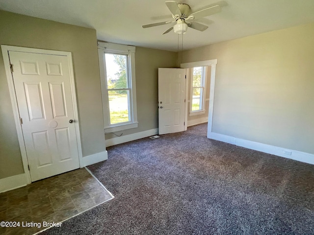 unfurnished bedroom with ceiling fan and dark colored carpet