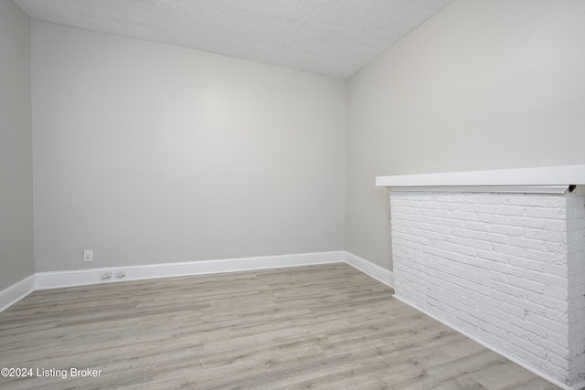 empty room featuring a textured ceiling, light hardwood / wood-style flooring, and lofted ceiling