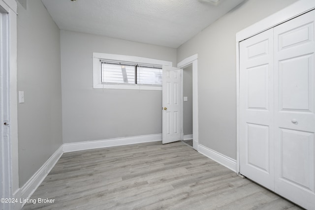 unfurnished bedroom featuring light hardwood / wood-style flooring, a textured ceiling, and a closet