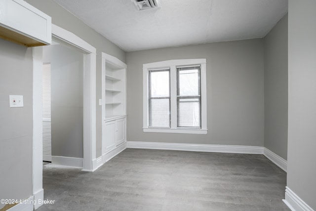 empty room featuring light hardwood / wood-style floors, a textured ceiling, and built in shelves