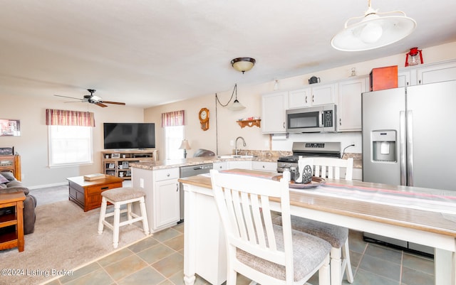 kitchen with hanging light fixtures, stainless steel appliances, sink, white cabinets, and ceiling fan