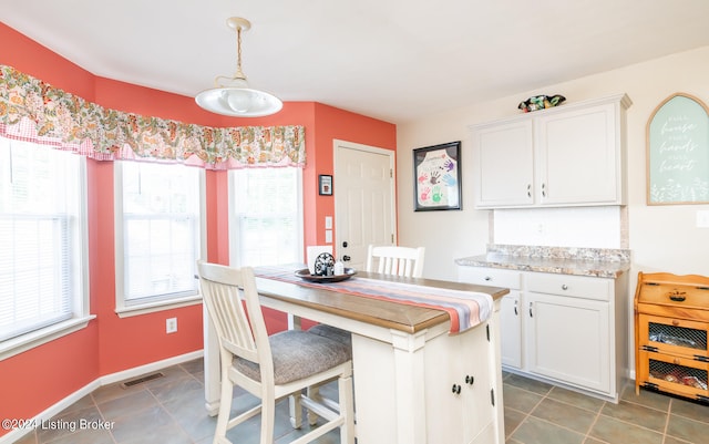 kitchen with white cabinetry, dark tile patterned floors, a kitchen breakfast bar, and hanging light fixtures