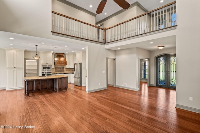 unfurnished living room featuring ornamental molding, ceiling fan, a towering ceiling, light hardwood / wood-style flooring, and french doors