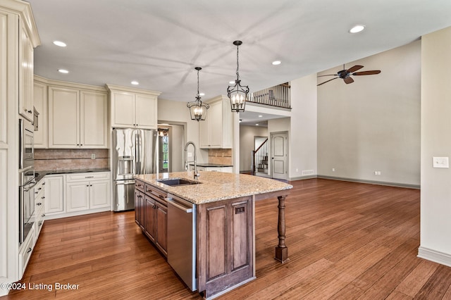 kitchen with a center island with sink, sink, appliances with stainless steel finishes, decorative light fixtures, and light wood-type flooring