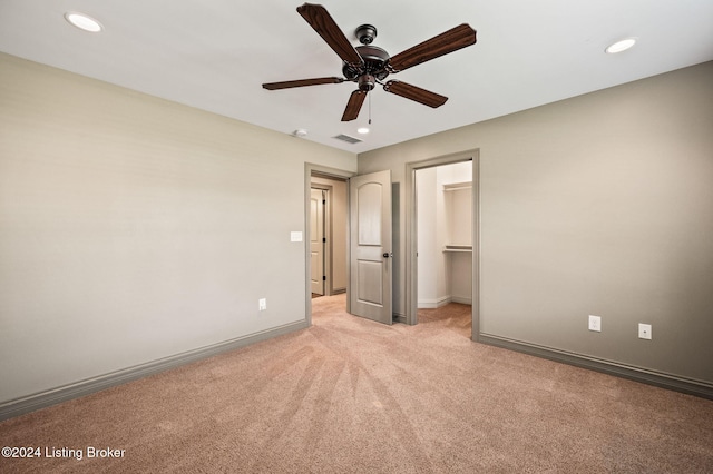 unfurnished bedroom with ceiling fan, a closet, a walk in closet, and light colored carpet