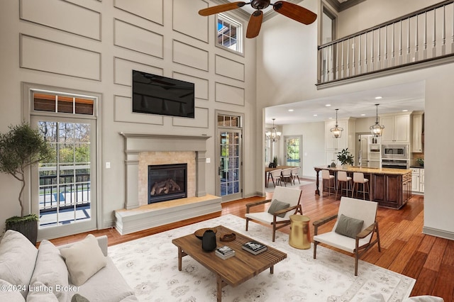 living room with a high ceiling, ceiling fan with notable chandelier, ornamental molding, and hardwood / wood-style flooring