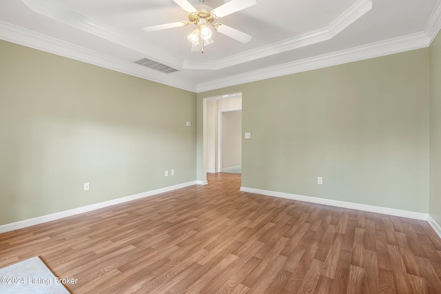 empty room with ornamental molding, ceiling fan, a tray ceiling, and light hardwood / wood-style floors