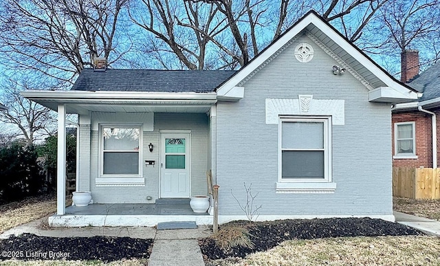 view of front of house featuring brick siding, a chimney, a shingled roof, and fence