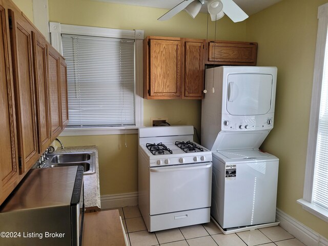 clothes washing area with sink, stacked washer / dryer, light tile patterned floors, and ceiling fan