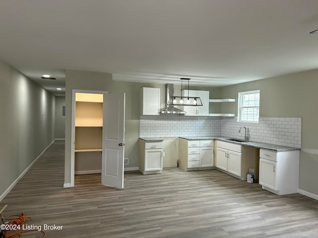 kitchen with wall chimney range hood, sink, light hardwood / wood-style floors, decorative light fixtures, and white cabinets