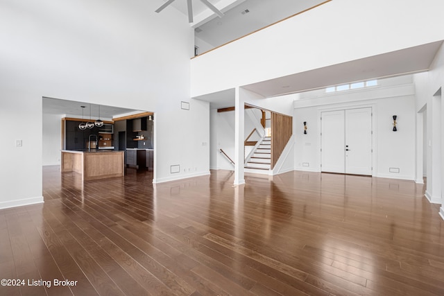 unfurnished living room featuring dark wood-type flooring, a high ceiling, and an inviting chandelier