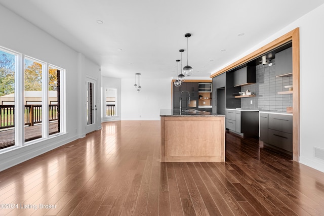 kitchen featuring hanging light fixtures, a center island with sink, dark hardwood / wood-style flooring, and tasteful backsplash