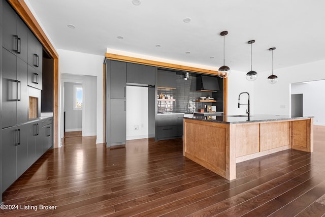 kitchen featuring tasteful backsplash, hanging light fixtures, an island with sink, and dark hardwood / wood-style floors