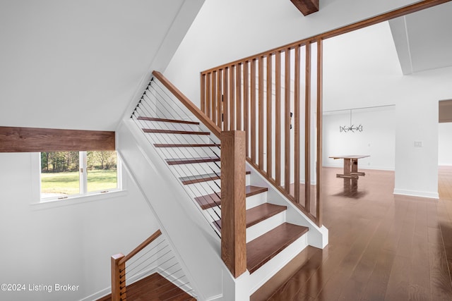 stairs with wood-type flooring, a high ceiling, and an inviting chandelier