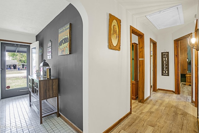 hall with arched walkways, light wood-style flooring, a textured ceiling, and baseboards