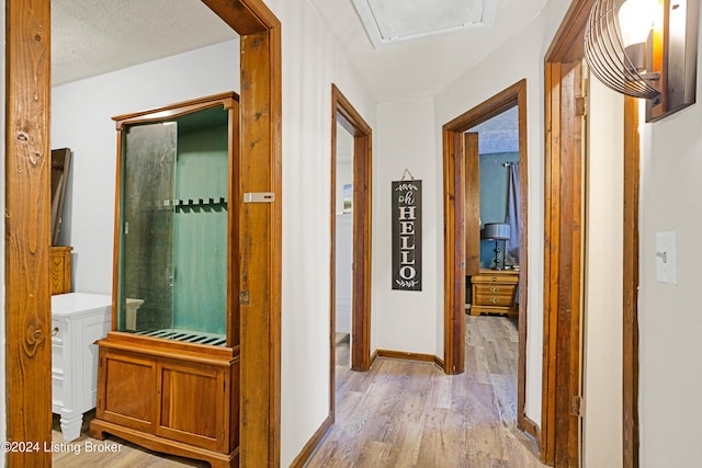 hallway featuring a textured ceiling, light wood-type flooring, and baseboards