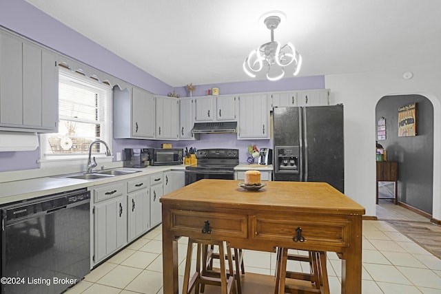 kitchen with black appliances, light tile patterned floors, under cabinet range hood, and a sink