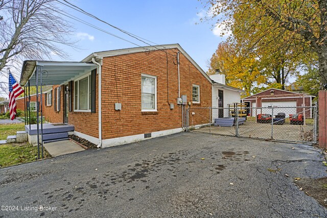 view of side of home with an outdoor structure, fence, brick siding, and driveway