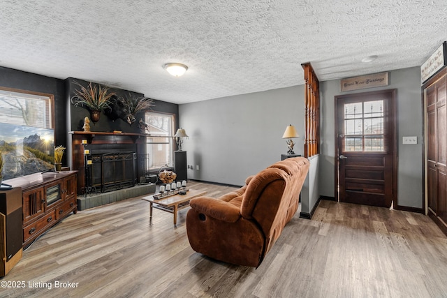 living room with baseboards, a textured ceiling, a fireplace with raised hearth, and light wood-style flooring