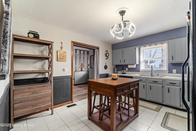 kitchen with visible vents, gray cabinets, a sink, light countertops, and a chandelier