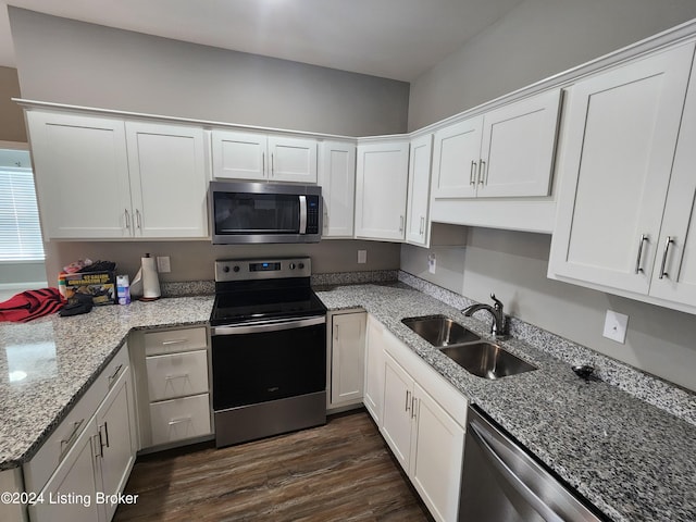 kitchen with stainless steel appliances, white cabinetry, sink, light stone counters, and dark hardwood / wood-style floors