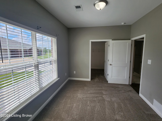 unfurnished bedroom with a closet, a walk in closet, and dark carpet