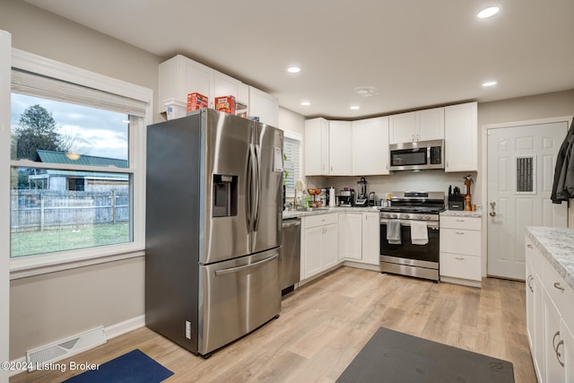 kitchen with stainless steel appliances, light stone countertops, sink, light hardwood / wood-style floors, and white cabinets