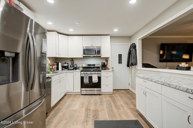 kitchen with light stone countertops, light hardwood / wood-style floors, white cabinetry, and appliances with stainless steel finishes