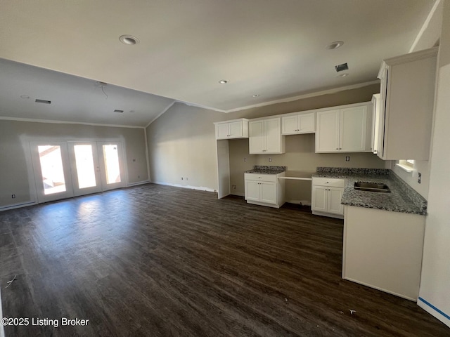 kitchen with dark wood-type flooring, dark stone counters, ornamental molding, and white cabinetry