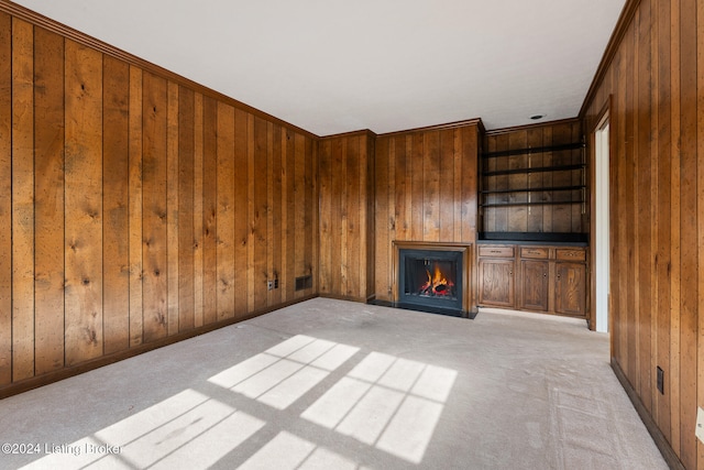 unfurnished living room featuring wood walls, built in features, light carpet, and crown molding