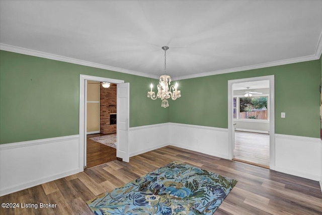 unfurnished dining area with ornamental molding, a fireplace, ceiling fan with notable chandelier, and wood-type flooring