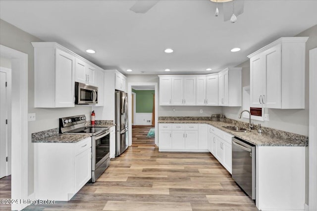 kitchen with white cabinetry, appliances with stainless steel finishes, stone counters, sink, and light hardwood / wood-style flooring