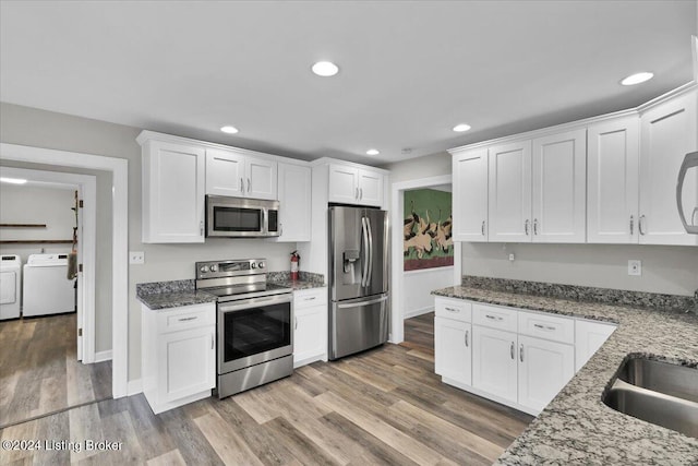 kitchen with stainless steel appliances, stone countertops, light hardwood / wood-style floors, white cabinetry, and washing machine and dryer