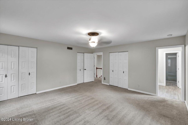 unfurnished bedroom featuring two closets, ensuite bathroom, ceiling fan, and carpet floors