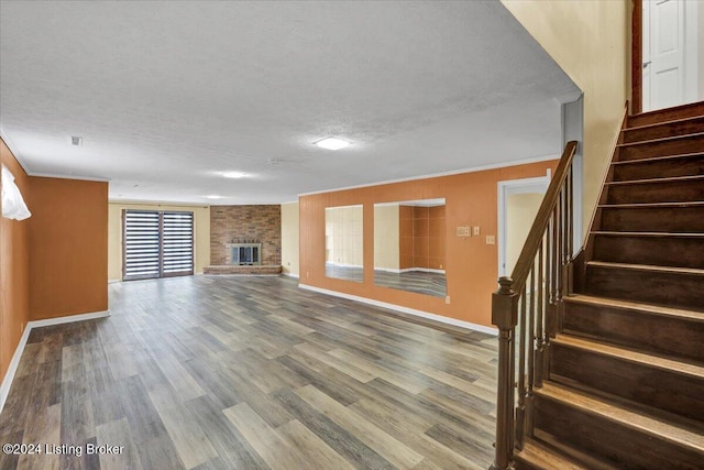 unfurnished living room with a textured ceiling, wood-type flooring, ornamental molding, and a fireplace