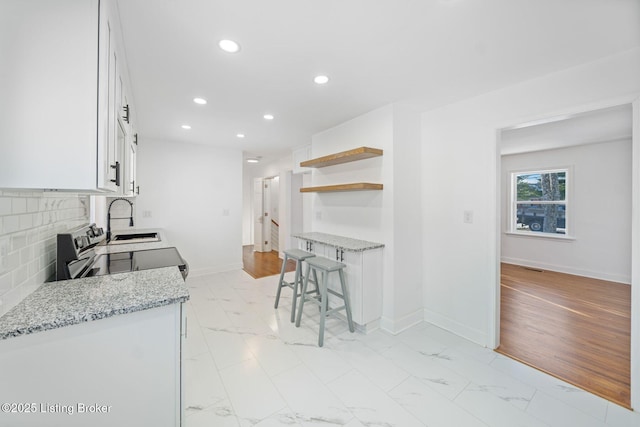 kitchen with tasteful backsplash, light stone countertops, white cabinets, and stainless steel electric range oven