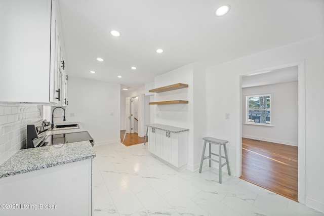 kitchen featuring sink, stainless steel electric range, backsplash, light stone counters, and white cabinets