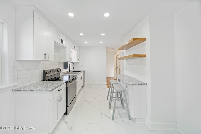 kitchen with sink, a kitchen breakfast bar, light stone counters, white cabinets, and stainless steel range with electric cooktop