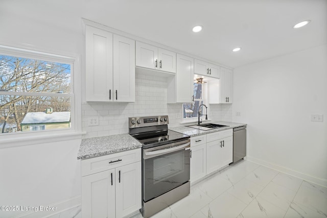 kitchen with tasteful backsplash, white cabinetry, sink, light stone counters, and stainless steel appliances