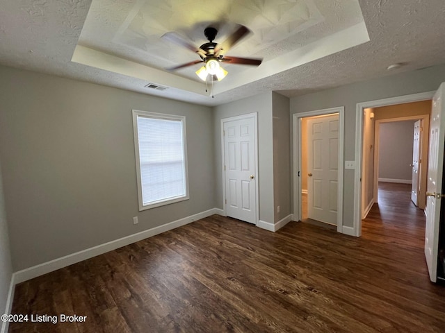 unfurnished bedroom with ceiling fan, a textured ceiling, dark hardwood / wood-style flooring, and a tray ceiling