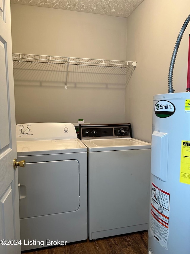 clothes washing area featuring electric water heater, a textured ceiling, washing machine and dryer, and dark wood-type flooring