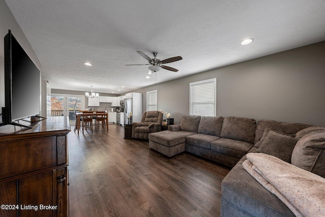 living room featuring ceiling fan with notable chandelier, a textured ceiling, and dark hardwood / wood-style flooring