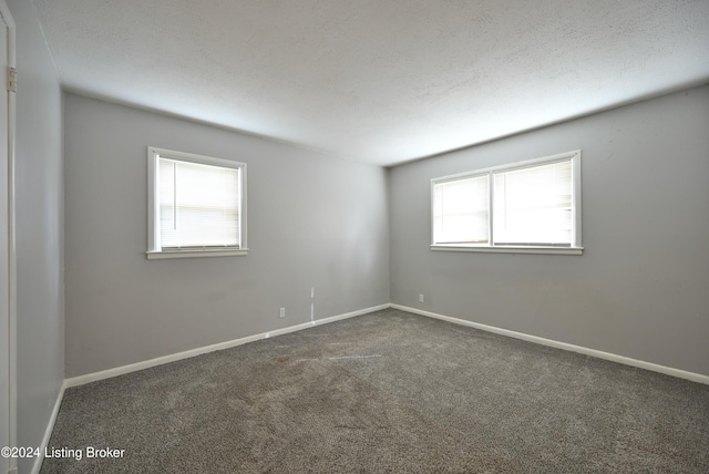 spare room with a wealth of natural light, a textured ceiling, and dark colored carpet