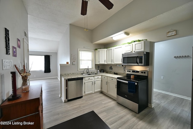 kitchen featuring stainless steel appliances, light wood-type flooring, white cabinetry, sink, and vaulted ceiling