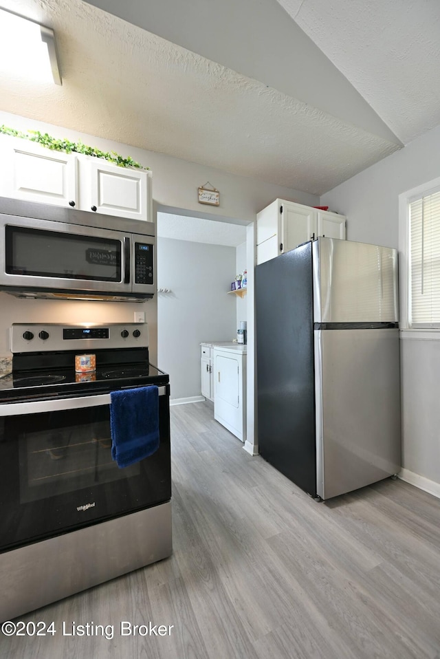 kitchen with light hardwood / wood-style floors, white cabinetry, appliances with stainless steel finishes, independent washer and dryer, and lofted ceiling