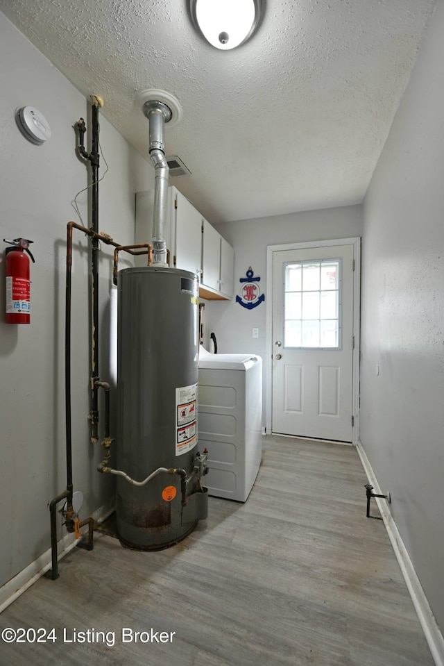 laundry area with light hardwood / wood-style floors, cabinets, water heater, a textured ceiling, and washer / dryer